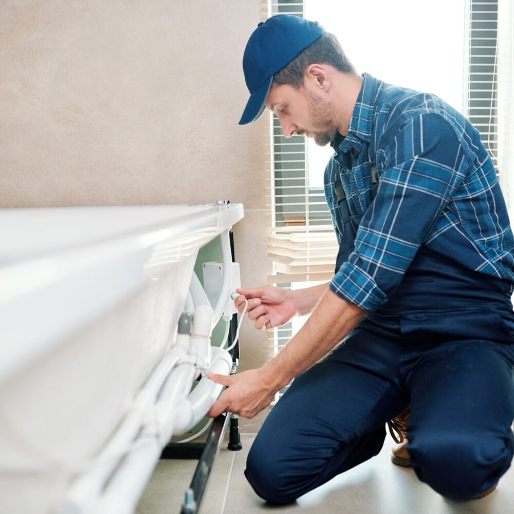 contemporary-technician-in-workwear-installing-pipe-system-by-bathtub