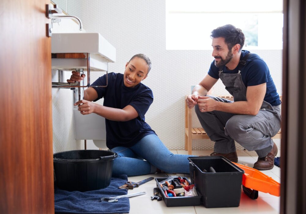 male-plumber-teaching-female-apprentice-to-fix-leaking-sink-in-home-bathroom