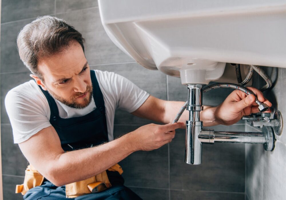 serious-male-plumber-in-working-overall-fixing-sink-in-bathroom